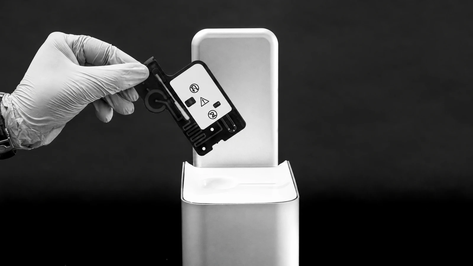 A hand inserts a rectangular cartridge into a compact upright reader.
