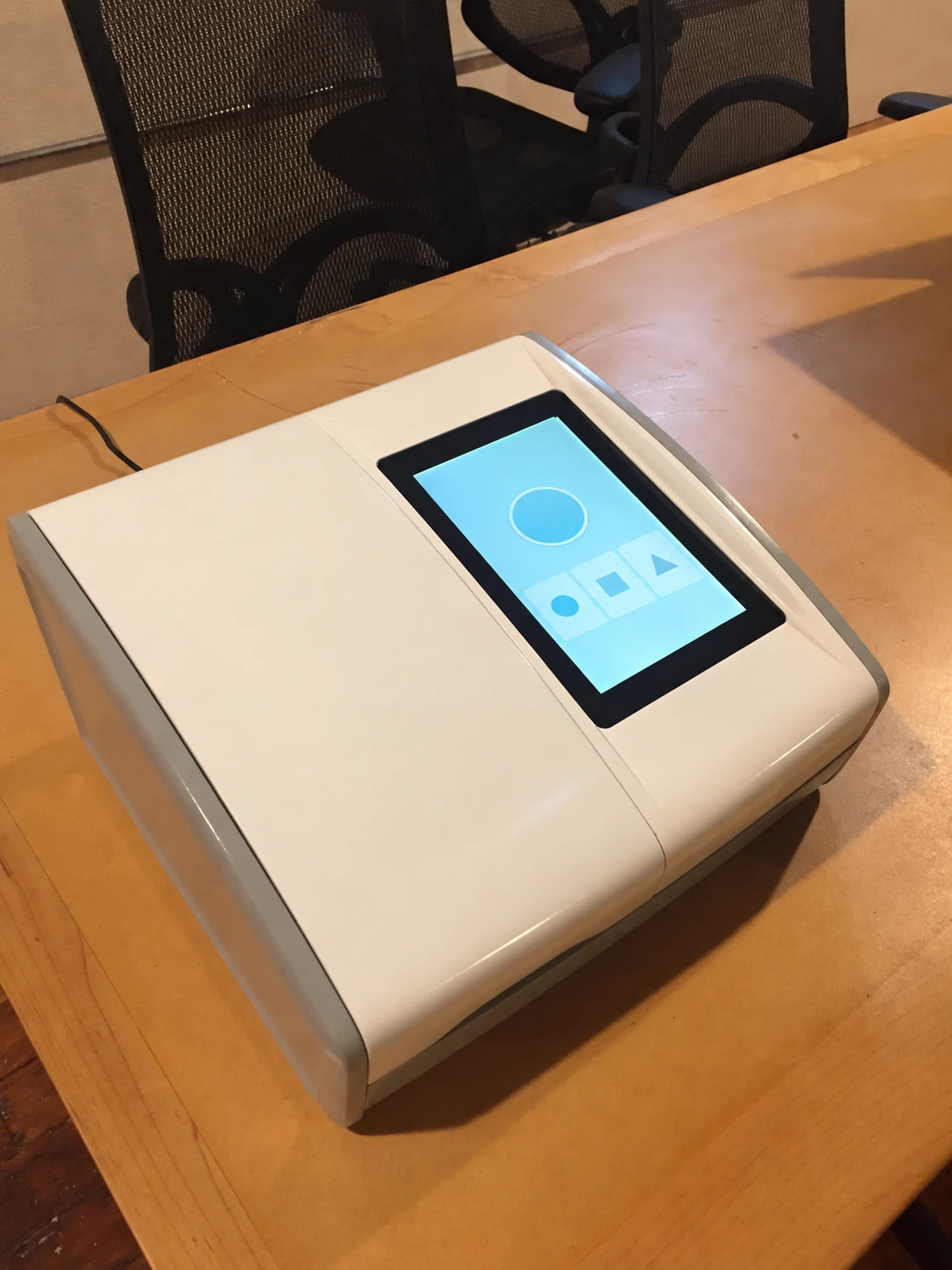 A pale tabletop instrument prototype with a sloped touchscreen on a workshop table.