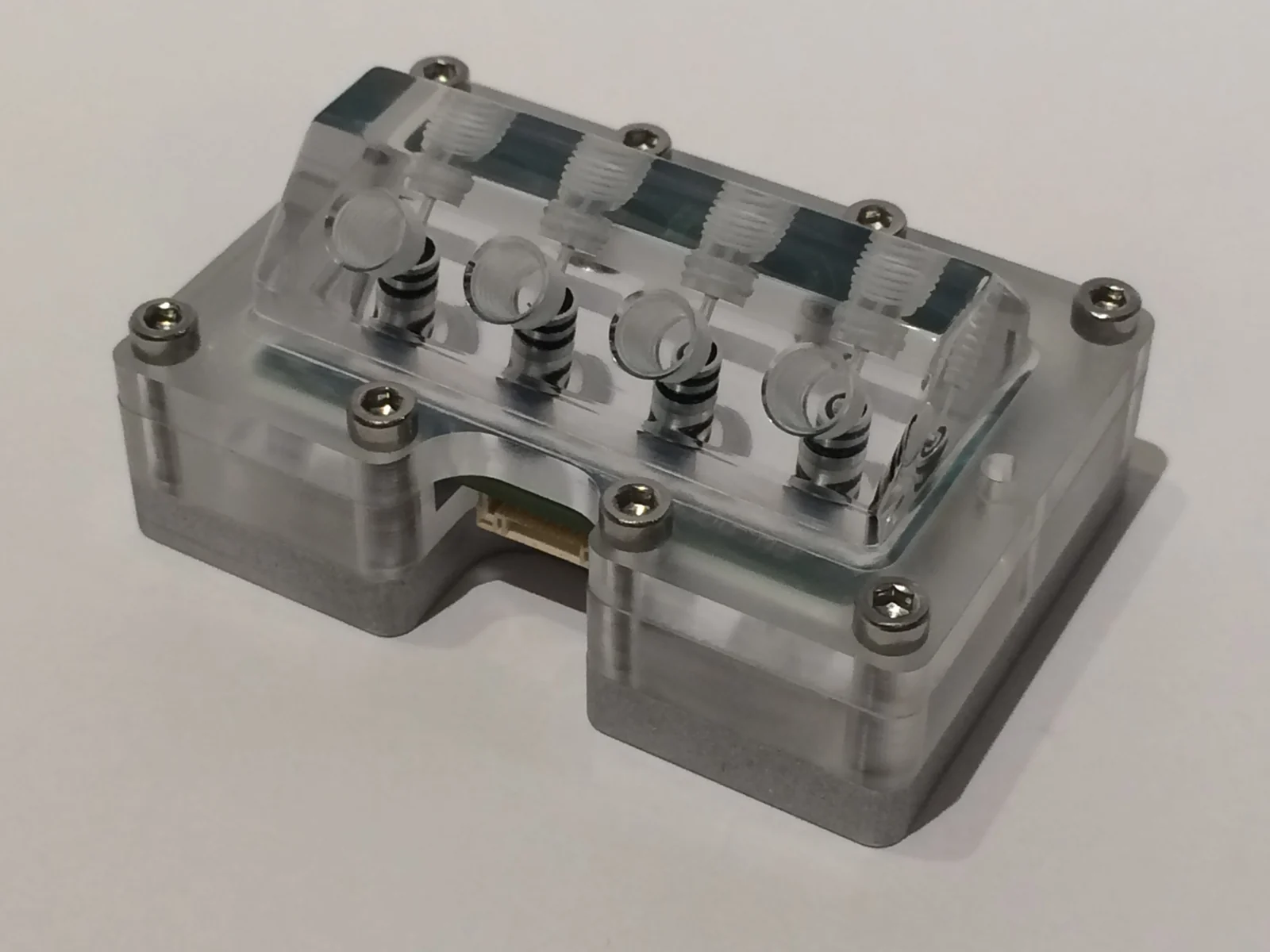 A clear acrylic assembly with threaded ports, seals, and metal fasteners.