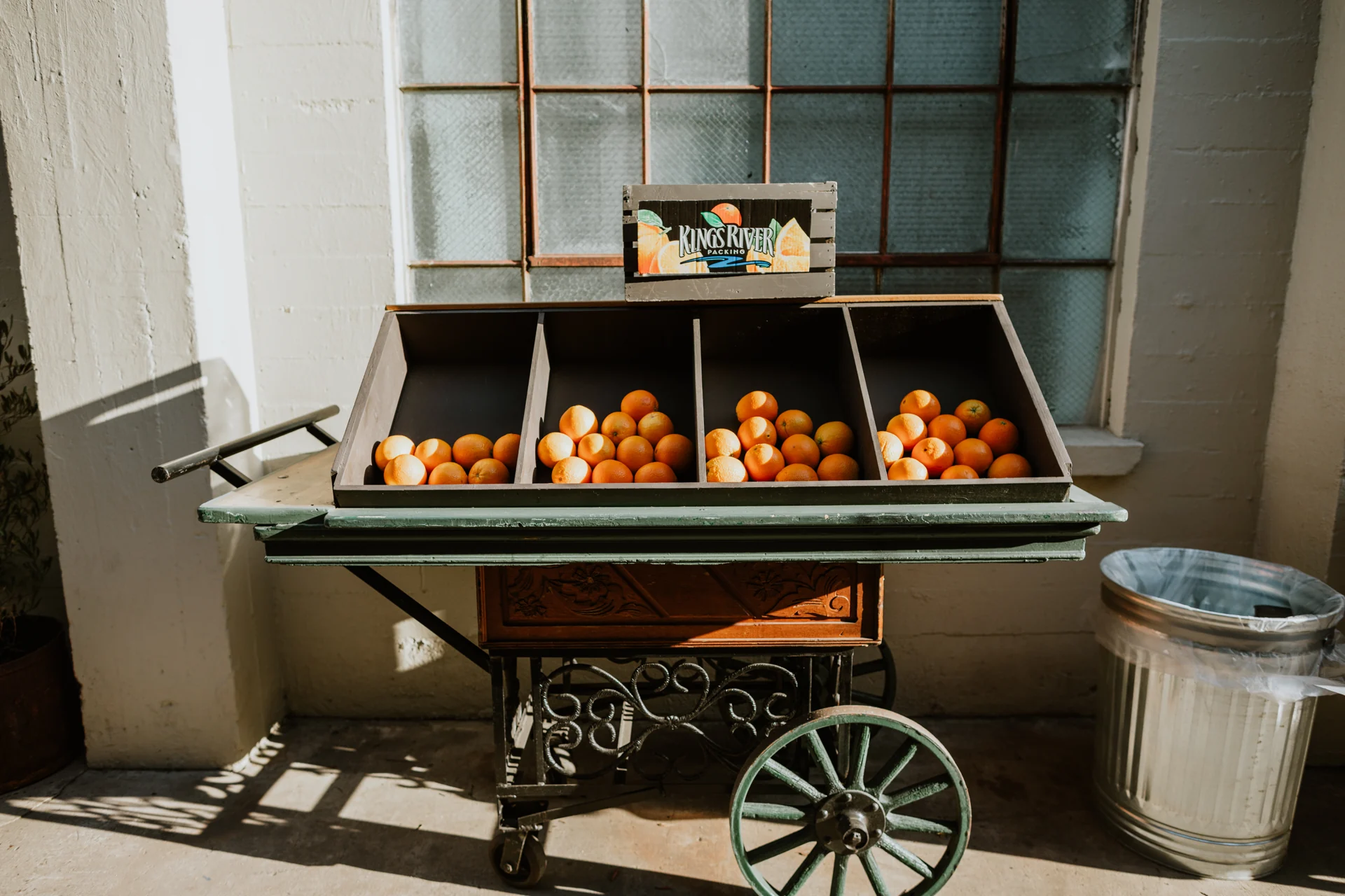 Oranges displayed in a vintage citrus cart beside industrial windows.