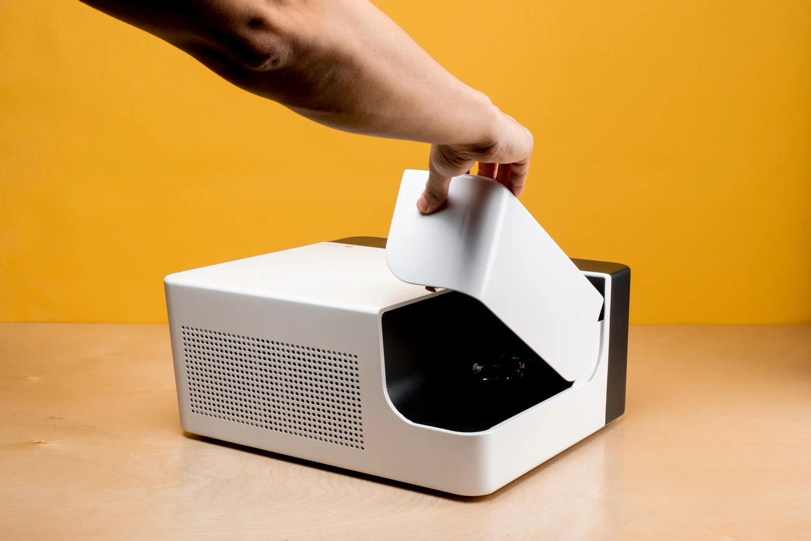 A hand lifts the white cover of a compact instrument on a warm orange background.