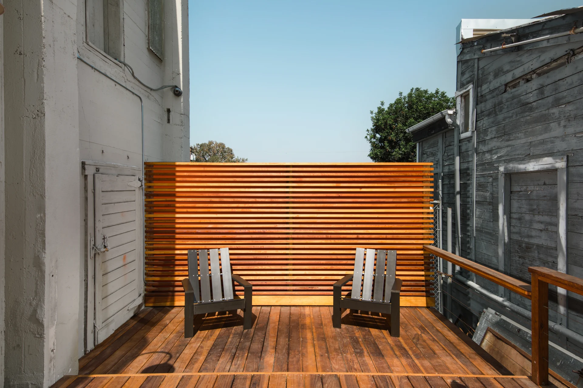Two chairs on a timber deck between historic industrial buildings.